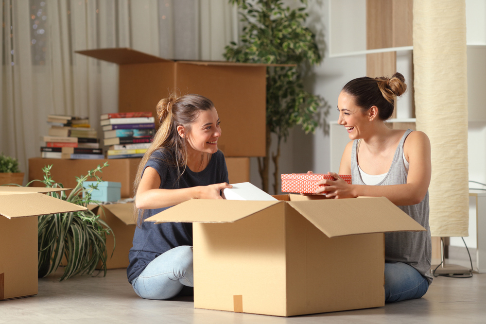 Two,Happy,Roommates,Talking,Unboxing,Gelongings,Moving,Home,Sitting,On
